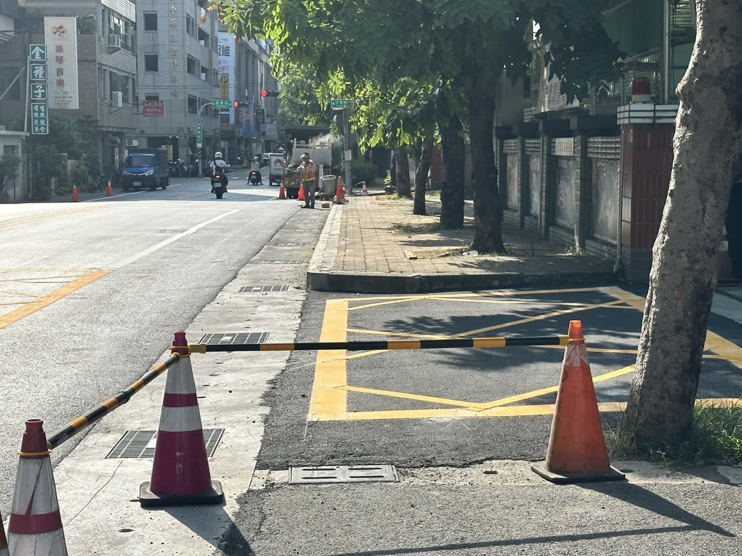 華興街沿線新鋪設的柏油路面與路側側溝蓋板，路口以交通錐管制，施工人員在遠端作業
